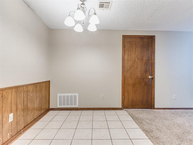 carpeted spare room featuring wood walls, an inviting chandelier, and a textured ceiling