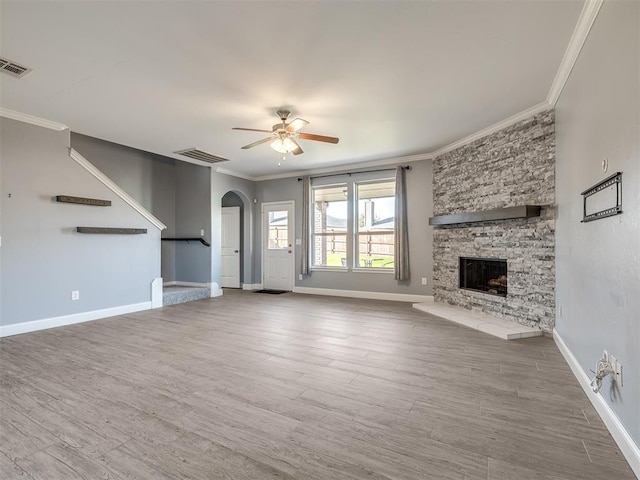 unfurnished living room with a stone fireplace, ceiling fan, crown molding, and hardwood / wood-style flooring