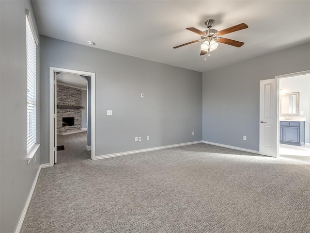 unfurnished bedroom featuring ceiling fan, a fireplace, light carpet, and ensuite bath