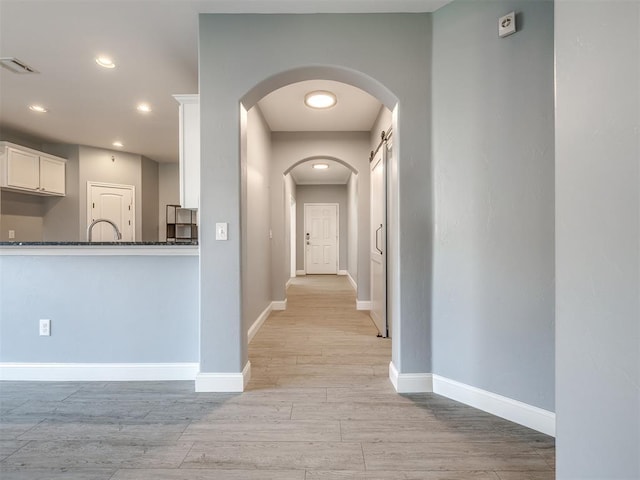 corridor with a barn door and light hardwood / wood-style floors