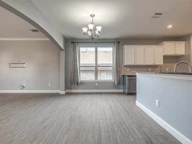 kitchen with sink, an inviting chandelier, tasteful backsplash, white cabinets, and light wood-type flooring