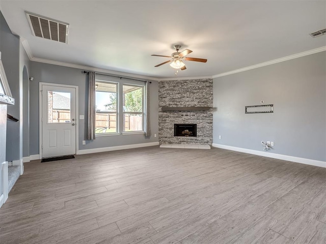 unfurnished living room featuring hardwood / wood-style flooring, ceiling fan, a stone fireplace, and crown molding