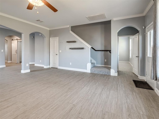 unfurnished living room with ceiling fan, a barn door, light hardwood / wood-style floors, and ornamental molding