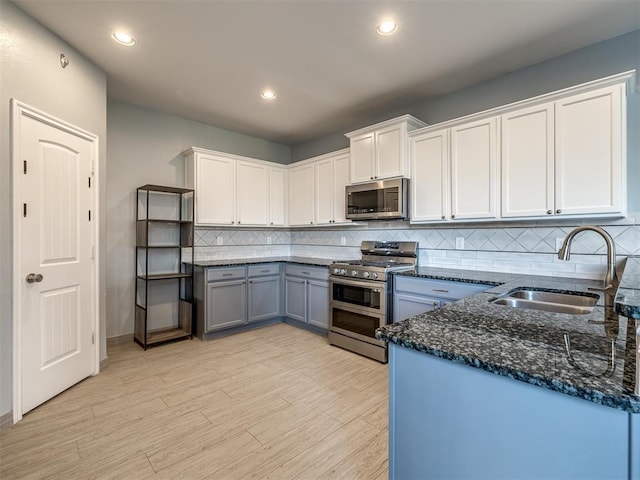 kitchen with backsplash, white cabinets, sink, appliances with stainless steel finishes, and light hardwood / wood-style floors