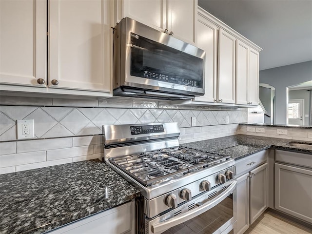 kitchen featuring white cabinets, sink, decorative backsplash, dark stone countertops, and stainless steel appliances