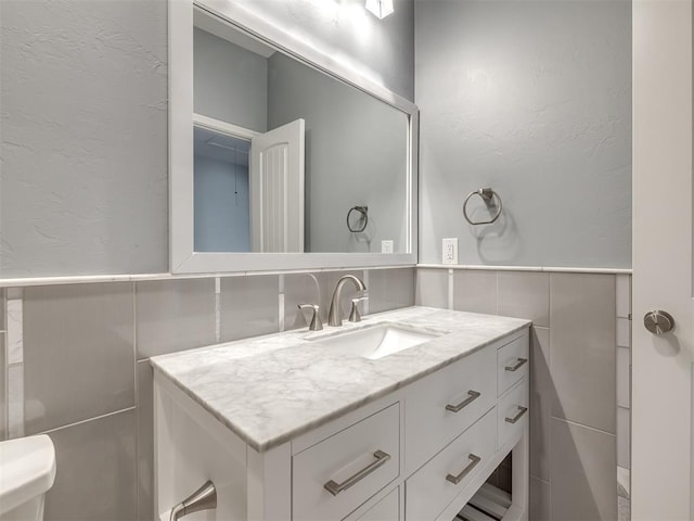 bathroom with vanity, toilet, and tile walls