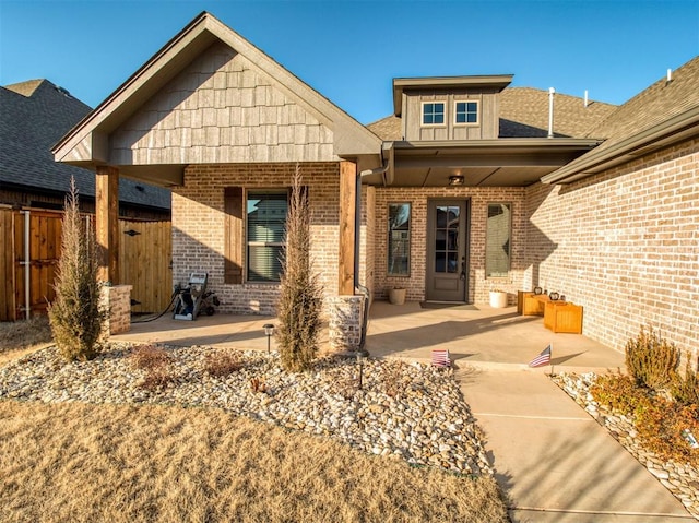 doorway to property featuring fence, a patio area, brick siding, and a shingled roof