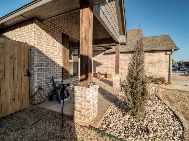 view of home's exterior with brick siding, a patio, and roof with shingles