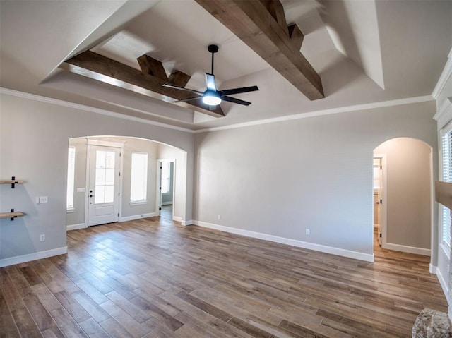 interior space with arched walkways, a raised ceiling, a healthy amount of sunlight, and wood finished floors