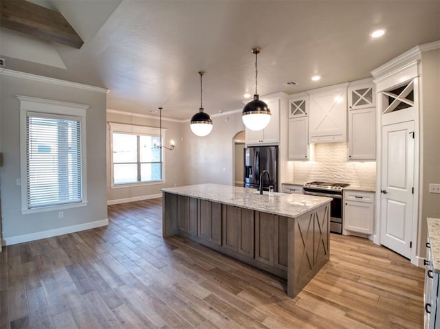 kitchen featuring tasteful backsplash, stainless steel range oven, black fridge, arched walkways, and white cabinetry