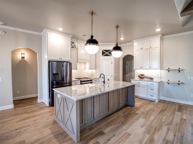 kitchen featuring arched walkways, white cabinets, appliances with stainless steel finishes, and a kitchen island with sink