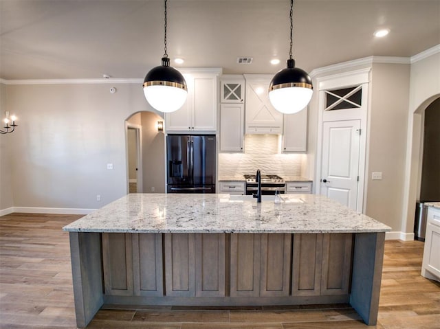 kitchen featuring stainless steel gas range oven, black fridge, arched walkways, white cabinets, and a sink