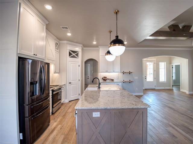 kitchen with stainless steel gas stove, visible vents, arched walkways, and black fridge with ice dispenser