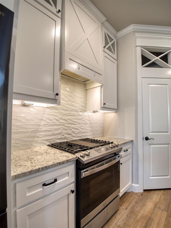 kitchen featuring backsplash, white cabinets, stainless steel gas range, and light wood-style flooring