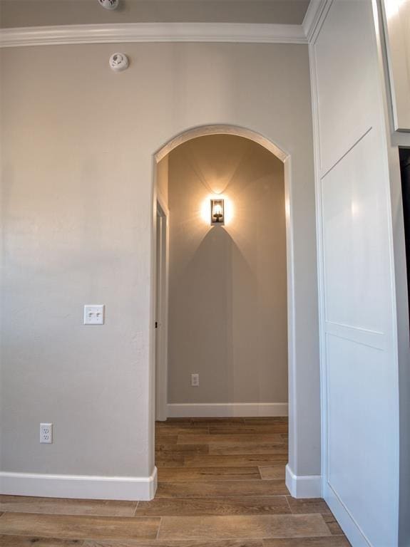 hall featuring arched walkways, ornamental molding, baseboards, and wood finished floors