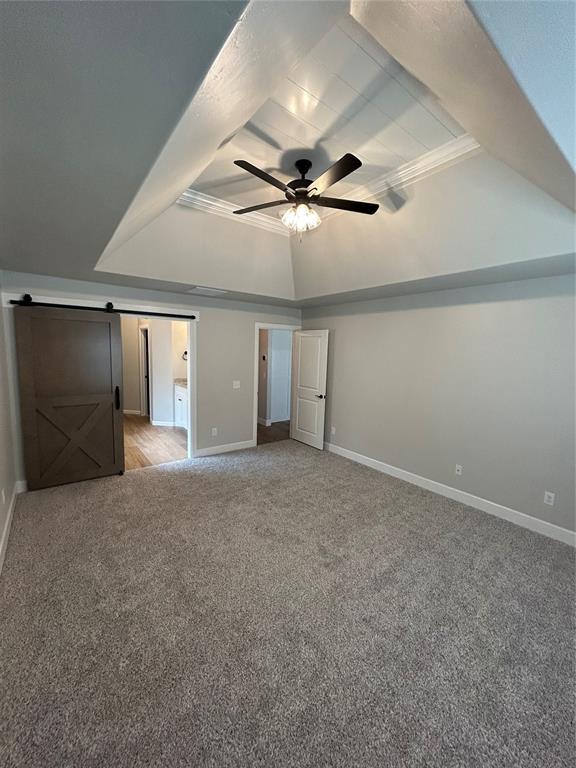 unfurnished bedroom featuring a ceiling fan, baseboards, a barn door, light colored carpet, and a raised ceiling