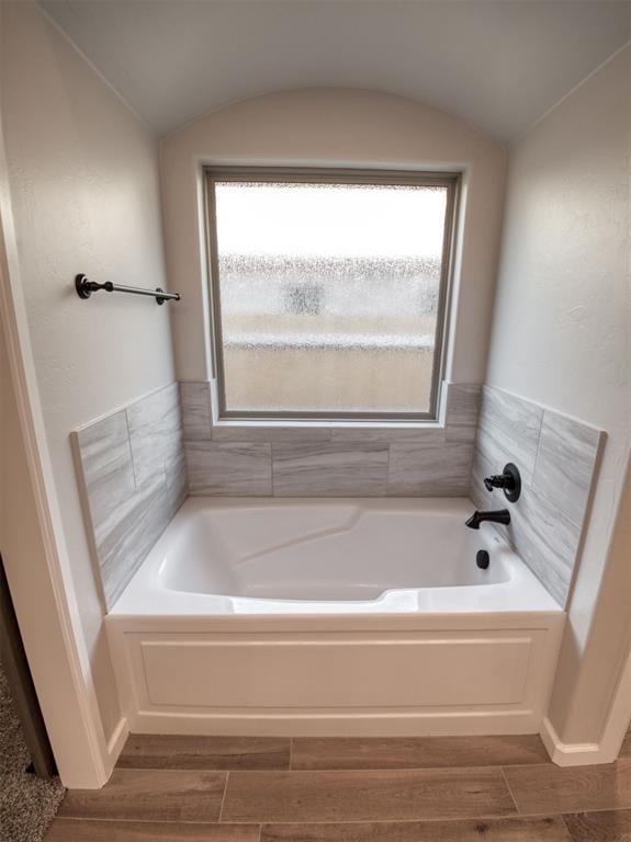 full bath featuring plenty of natural light, a garden tub, wood finish floors, and vaulted ceiling