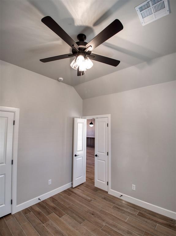 unfurnished bedroom with visible vents, ceiling fan, baseboards, vaulted ceiling, and wood finished floors