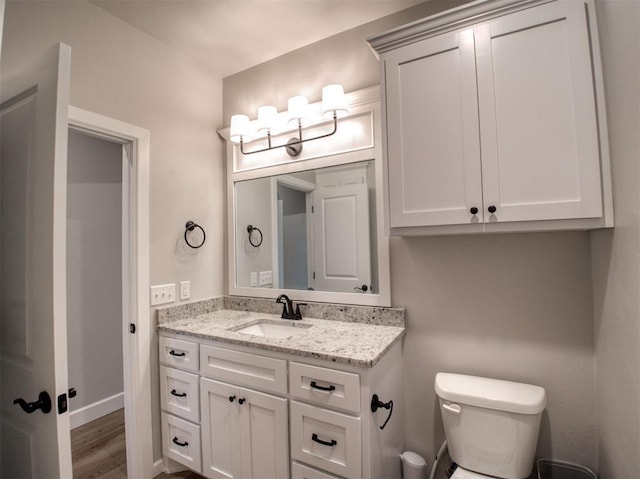 bathroom featuring baseboards, toilet, wood finished floors, and vanity