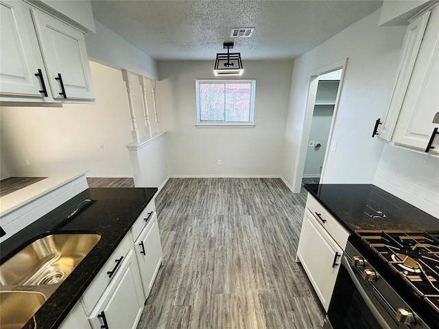 kitchen featuring dark stone counters, stainless steel gas range, a textured ceiling, sink, and white cabinets