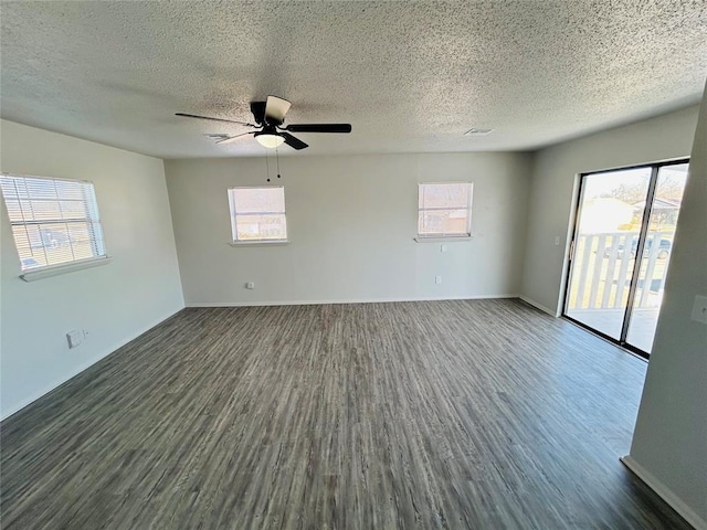 empty room with a textured ceiling, plenty of natural light, ceiling fan, and dark wood-type flooring