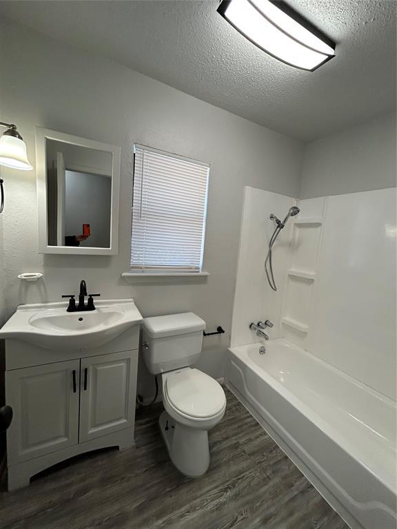 full bathroom with a textured ceiling, toilet, shower / washtub combination, vanity, and hardwood / wood-style flooring