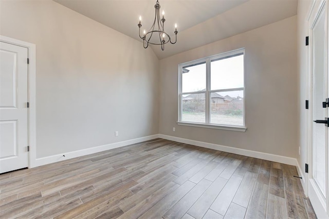 empty room with light hardwood / wood-style floors, lofted ceiling, and a notable chandelier