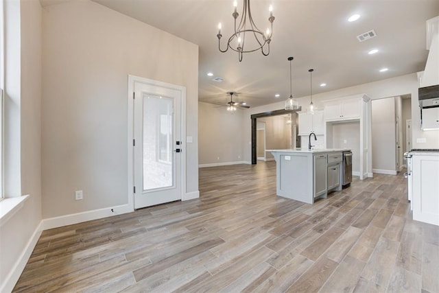 kitchen with ceiling fan with notable chandelier, a kitchen island with sink, pendant lighting, light hardwood / wood-style flooring, and white cabinetry