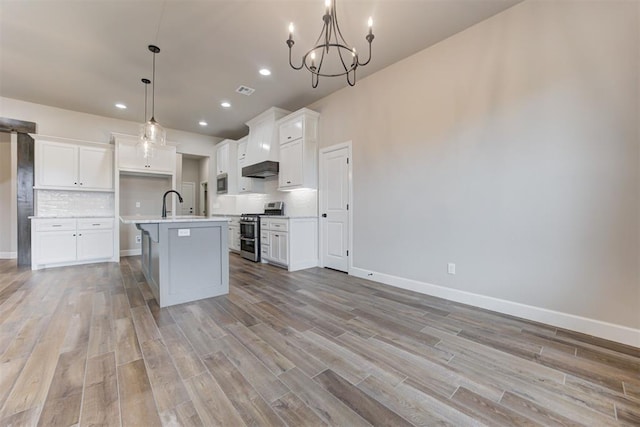 kitchen with appliances with stainless steel finishes, light wood-type flooring, a kitchen island with sink, decorative light fixtures, and white cabinets