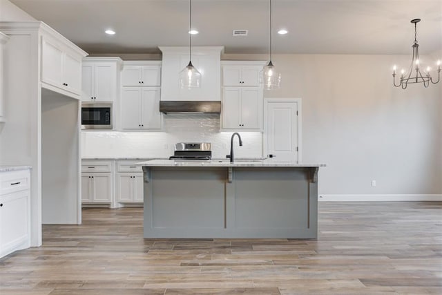 kitchen with sink, hanging light fixtures, stainless steel stove, built in microwave, and white cabinetry