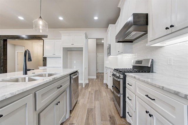 kitchen featuring white cabinets, stainless steel appliances, hanging light fixtures, and wall chimney range hood