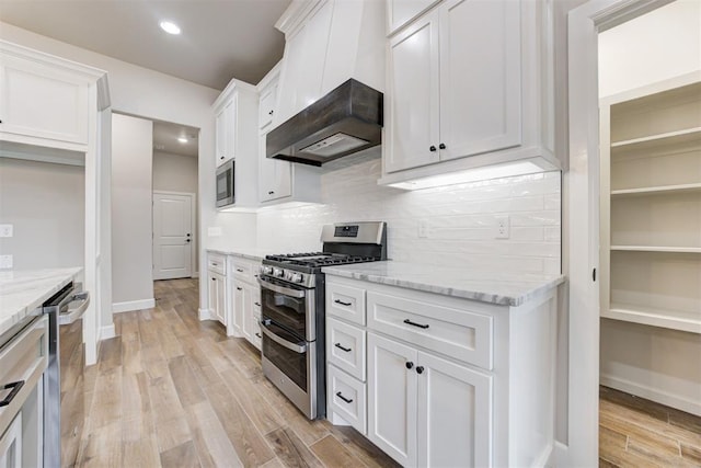 kitchen with stainless steel appliances, light stone counters, decorative backsplash, white cabinets, and light wood-type flooring