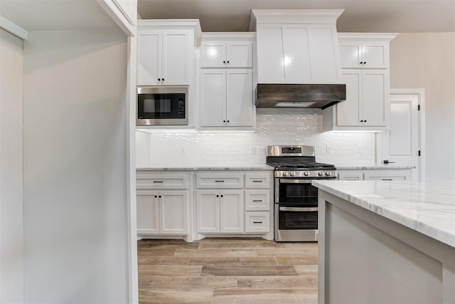 kitchen featuring gas range, white cabinetry, built in microwave, light stone counters, and backsplash