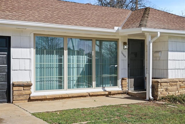 entrance to property featuring stone siding and a shingled roof