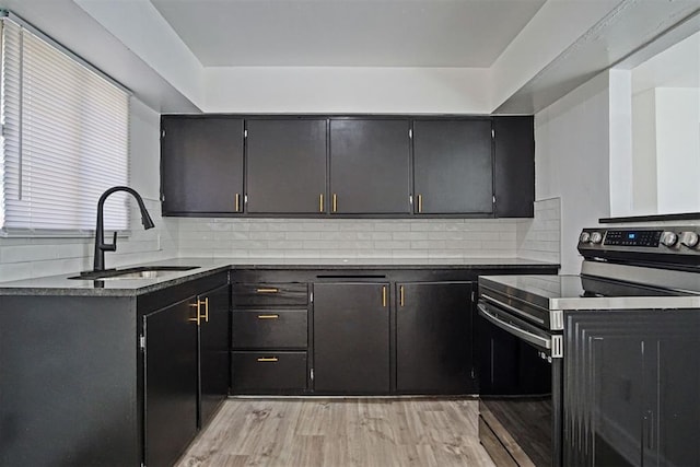 kitchen with a sink, dark countertops, stainless steel electric range, and light wood-style flooring