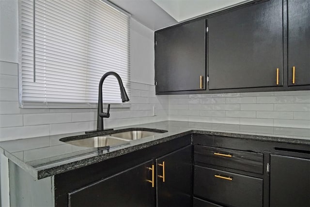 kitchen with tasteful backsplash, dark stone counters, dark cabinetry, and a sink