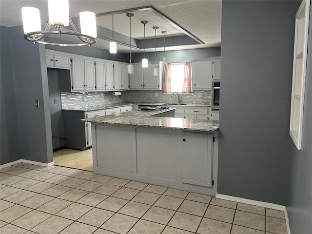 kitchen featuring light stone countertops, stainless steel oven, hanging light fixtures, a raised ceiling, and light tile patterned floors