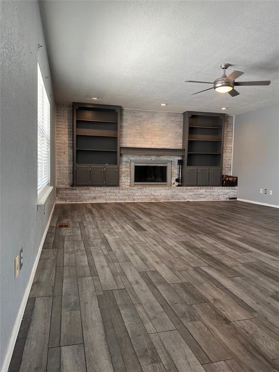 unfurnished living room with built in shelves, dark hardwood / wood-style floors, a textured ceiling, and a brick fireplace