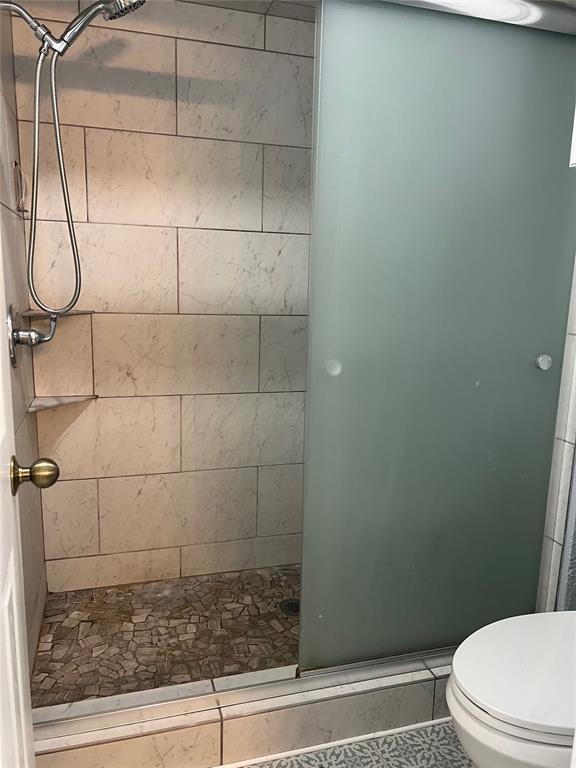 bathroom featuring tile patterned flooring, toilet, and a tile shower