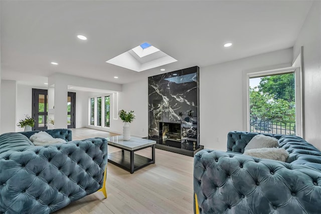 living room with a high end fireplace, a skylight, and light hardwood / wood-style flooring