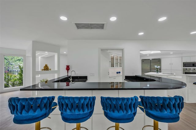 kitchen with a kitchen bar, sink, built in appliances, white cabinetry, and a large island