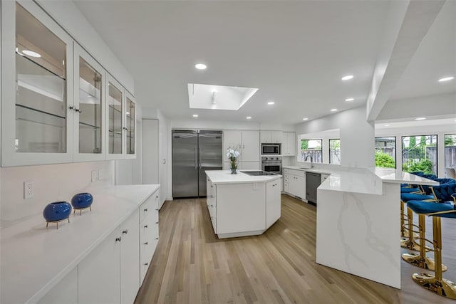 kitchen featuring backsplash, a skylight, built in appliances, white cabinetry, and a large island