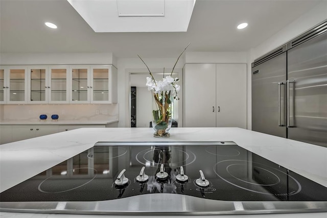 kitchen with white cabinets, stainless steel built in fridge, black electric stovetop, and a skylight