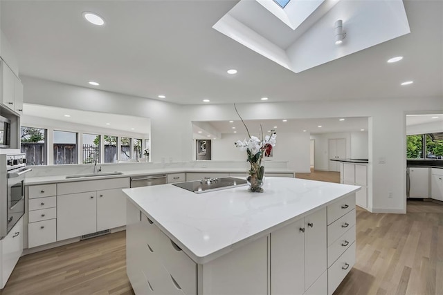 kitchen with a wealth of natural light, a center island, white cabinets, and appliances with stainless steel finishes