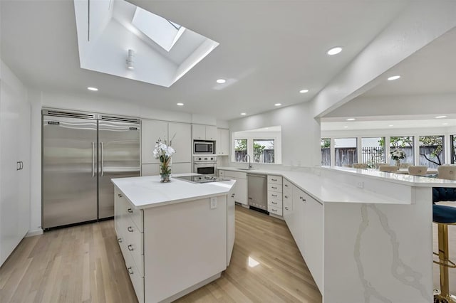 kitchen with a breakfast bar area, built in appliances, kitchen peninsula, and white cabinets