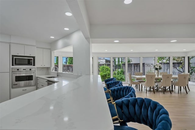 kitchen with stainless steel oven, white cabinets, sink, built in microwave, and light stone counters