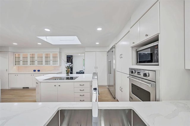 kitchen with built in appliances, light stone countertops, white cabinets, and a skylight