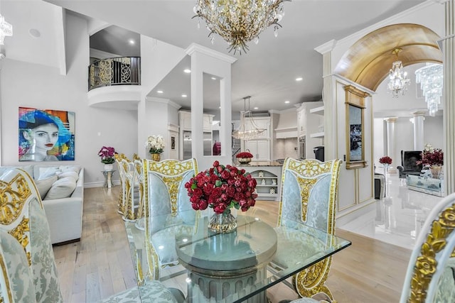 dining space with an inviting chandelier, ornate columns, ornamental molding, and light hardwood / wood-style flooring