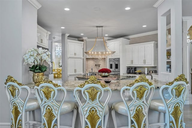 kitchen featuring kitchen peninsula, tasteful backsplash, light stone counters, white cabinetry, and hanging light fixtures