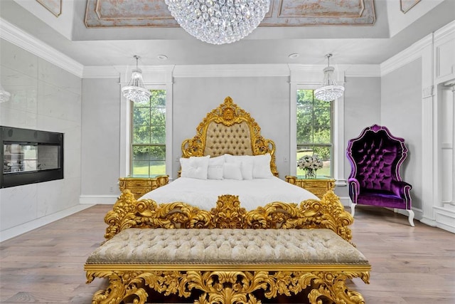 bedroom with a tray ceiling, a tile fireplace, light hardwood / wood-style flooring, and ornamental molding